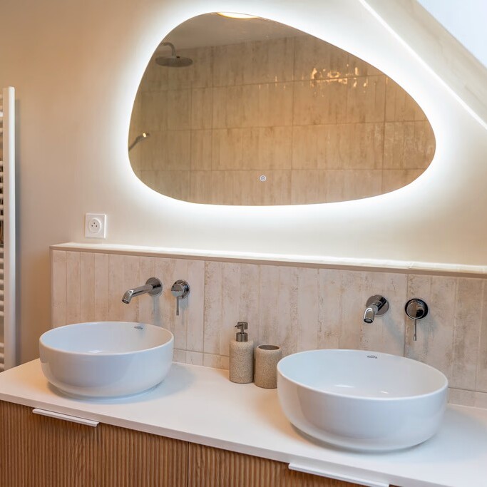 Espace lavabo rénové avec vasques blanches, robinetterie murale et éclairage design.