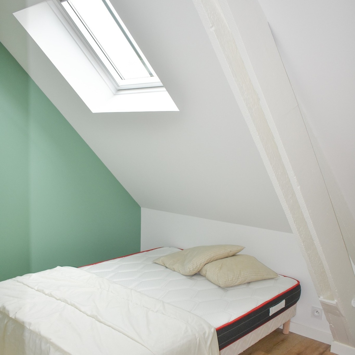 Aménagement d’une chambre sous toiture avec fenêtre de toit et finitions modernes.