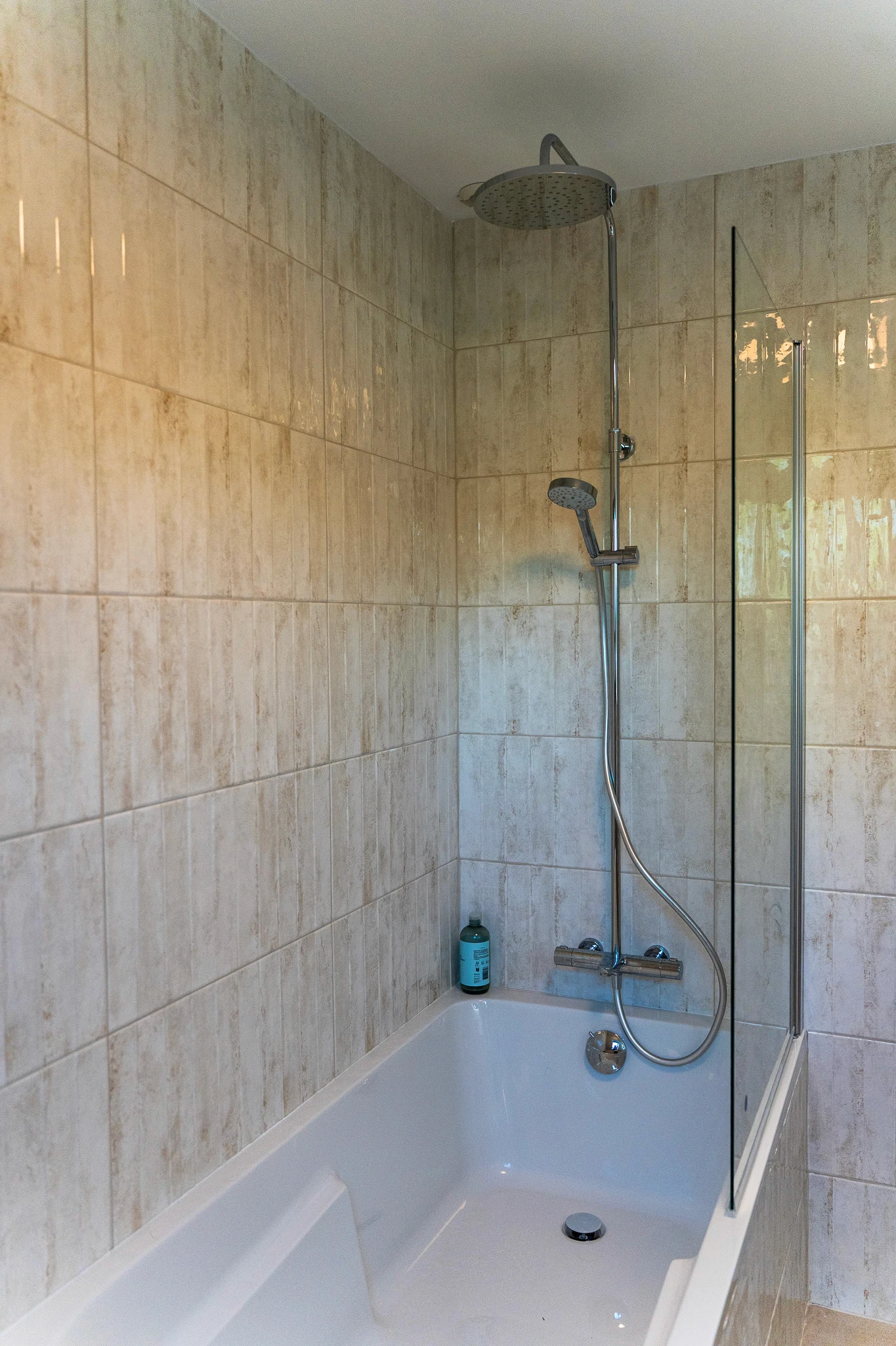 Douche installée au-dessus d’une baignoire avec colonne de douche et paroi en verre, dans une salle de bain moderne