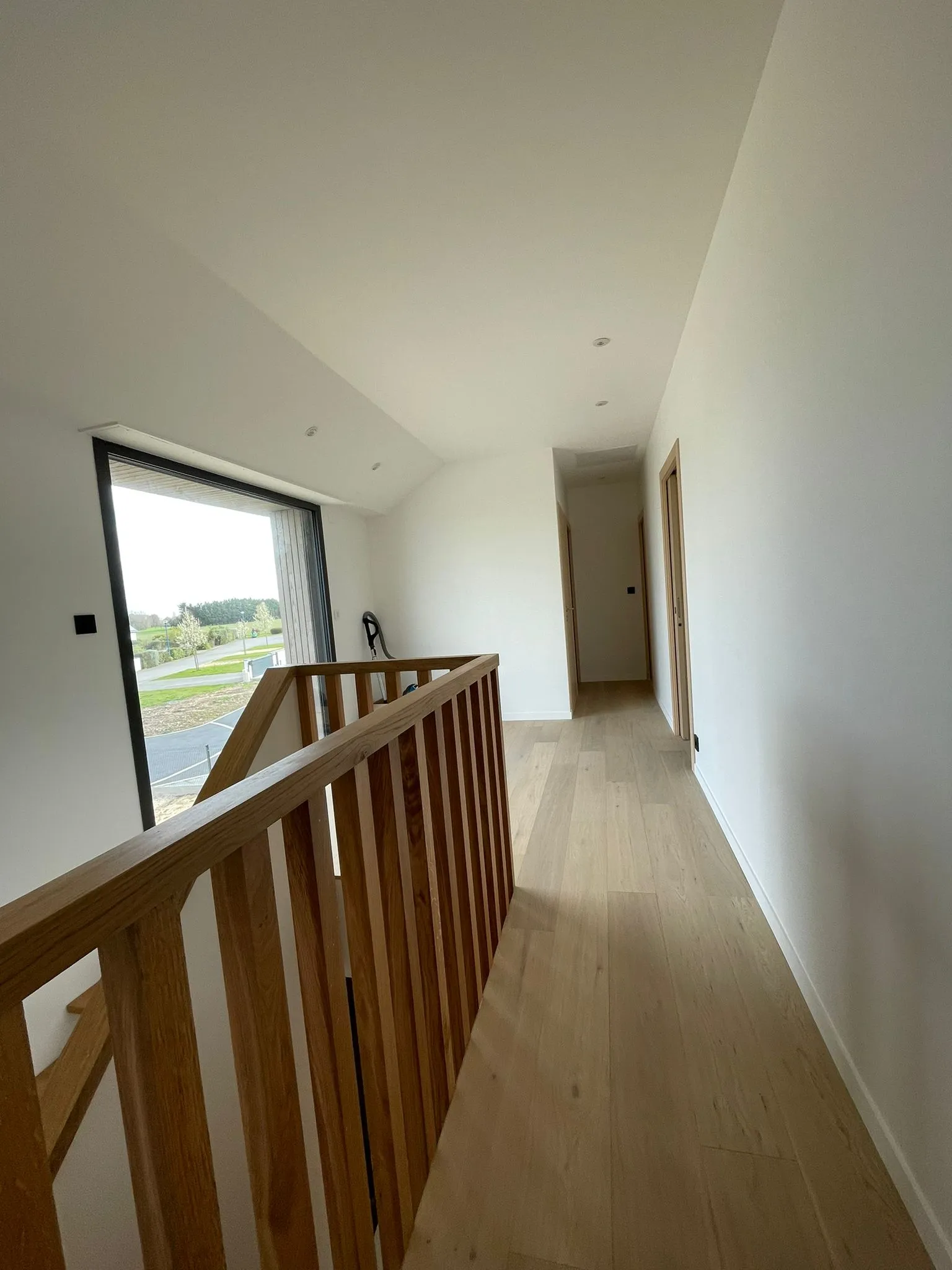 Couloir lumineux rénové à l’étage, avec garde-corps en bois et accès aux chambres.