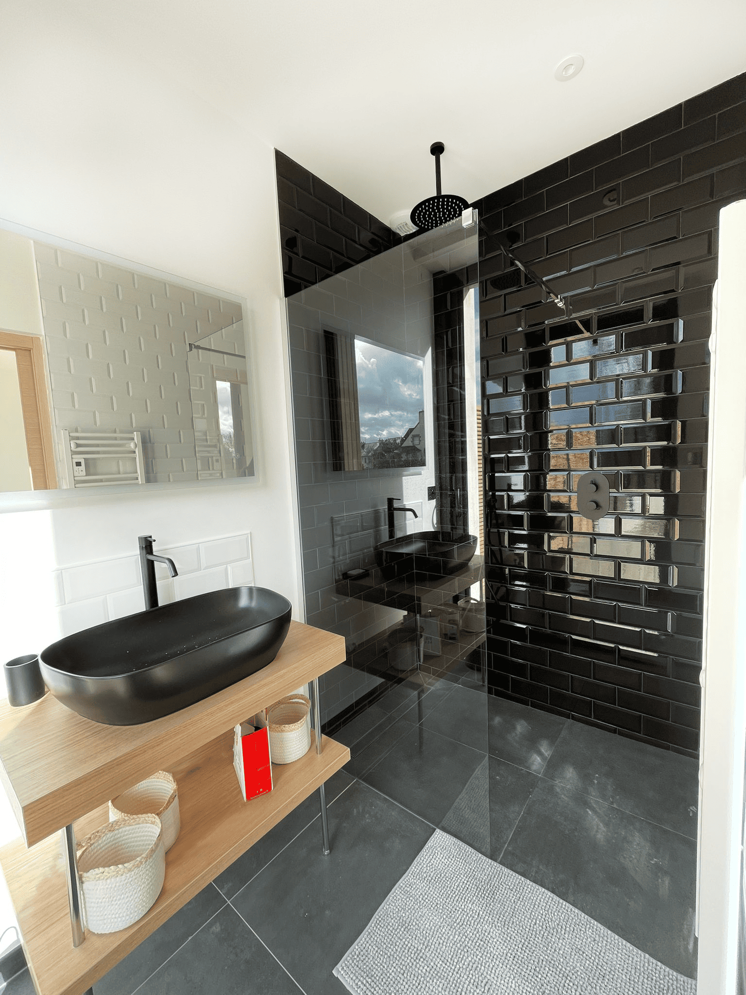 Rénovation de salle de bain moderne avec douche vitrée, vasque noire et carrelage mural métro noir brillant.